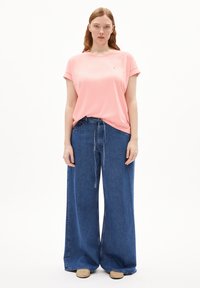 T-shirt di cotone rosa con maniche arrotolate, abbinata a pantaloni in denim blu a gamba larga. I pantaloni presentano una vita con cintura e una vestibilità comoda.