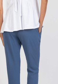 White peplum top with a tie detail at the back; paired with blue stretch trousers featuring side pockets and a smooth texture.
