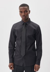 Camisa de vestir negra en un diseño ajustado, con collar clásico y cierre de botones, combinada con una corbata negra a juego, de textura suave.