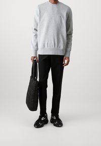 Grå sweatshirt med ribbede manchetter og kant, sorte bukser og en struktureret sort tote bag, suppleret med sorte sneakers med refleksdetaljer.