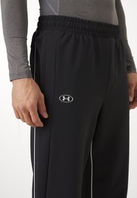 Sorte treningsbukser med elastisk midje, med hvite sidestreker og en liten grå logo på venstre lår. Laget av strukturert stoff.