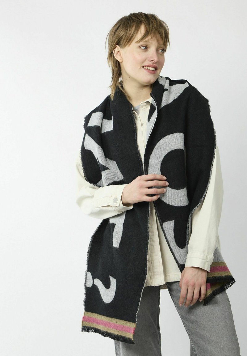 Écharpe en laine noire avec de grands motifs en texte blanc, bords frangés, et un accent rayé coloré en rose et or le long du bas.