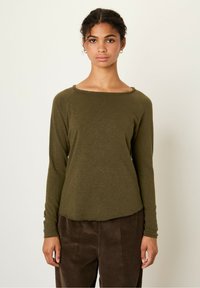Olive green long-sleeve shirt with a wide neckline and raw edge detail, paired with brown corduroy pants featuring vertical stripes.