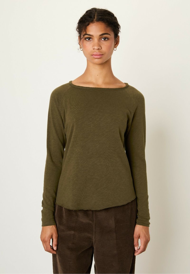 Olive green long-sleeve shirt with a wide neckline and raw edge detail, paired with brown corduroy pants featuring vertical stripes.