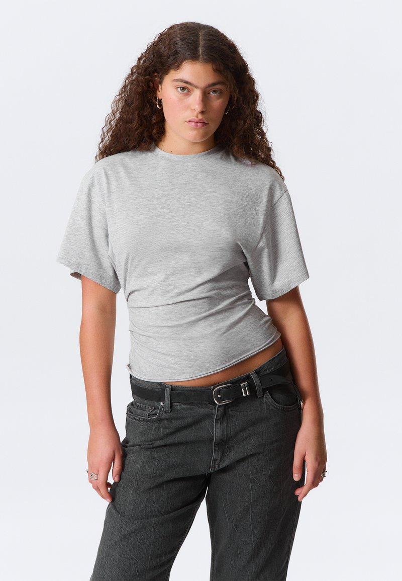 Tricou gri cu mâneci scurte, decolteu rotund și croială lejeră, realizat dintr-o țesătură fină, asortat cu pantaloni din denim închis. Accesoriu centură neagră.