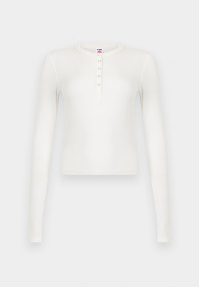 Λευκό μακρυμάνικο πλεκτό τοπ με ριμπ ύφασμα, στρογγυλή λαιμόκοψη και κουμπωτό πατιλέτα με πέντε μικρά κουμπιά, παρουσιάζεται σε λευκό φόντο.