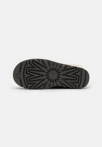 Suela de zapato de goma negra con un diseño de relieve en el patrón, con líneas radiales y un elemento central circular, que ofrece tracción y soporte.