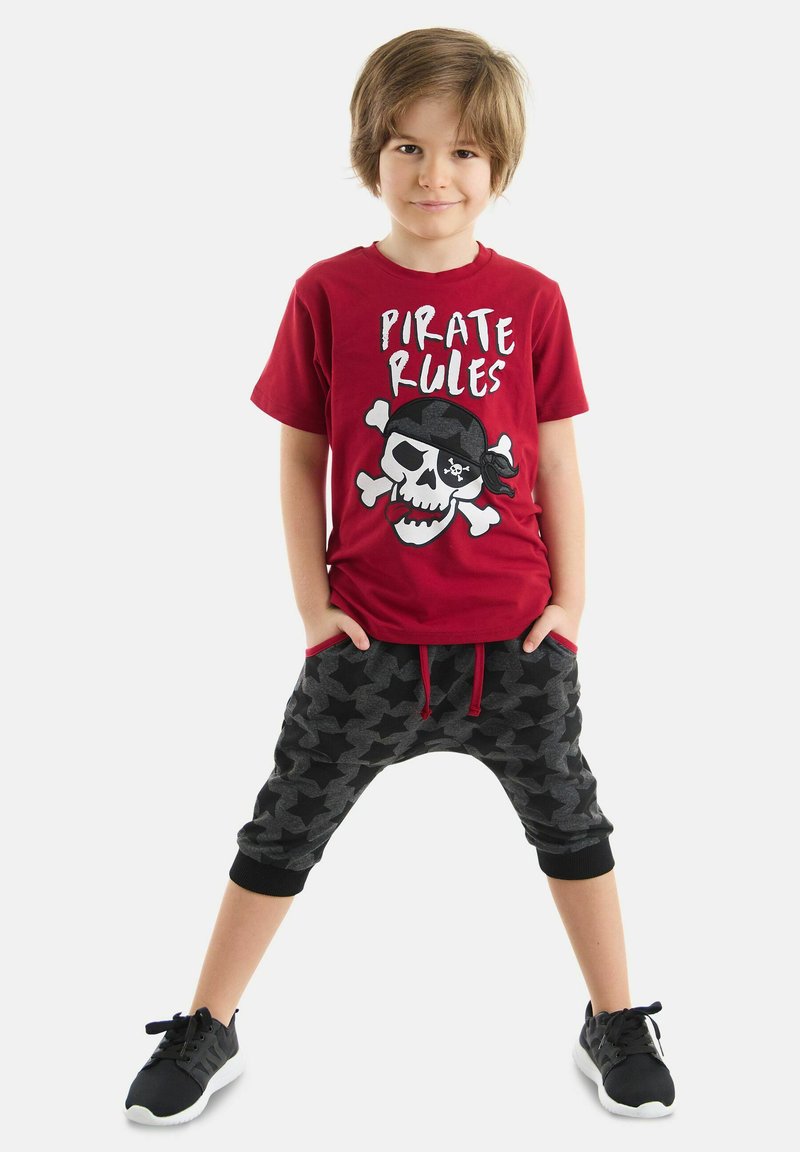 Rød bomulds t-shirt med grafik og design af et kranie med teksten "Pirate Rules". Sorte og grå joggerbukser med stjernemønster og lommer, sorte sneakers.