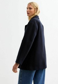 Abrigo de mezcla de lana color navy con un diseño entallado, cuello con muescas y mangas anchas, combinado con jeans de tiro alto en azul claro.