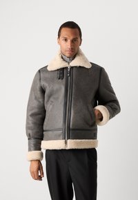 Δερμάτινο μπουφάν shearling σε σκούρο γκρι χρώμα με μπεζ γιακά και μανσέτες shearling, διαθέτοντας κλείσιμο με φερμουάρ και δύο πλαϊνές τσέπες.