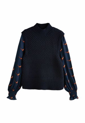 Pull sans manches en maille bleu marine superposé sur un chemisier bleu foncé à manches longues avec un imprimé oiseau orange.