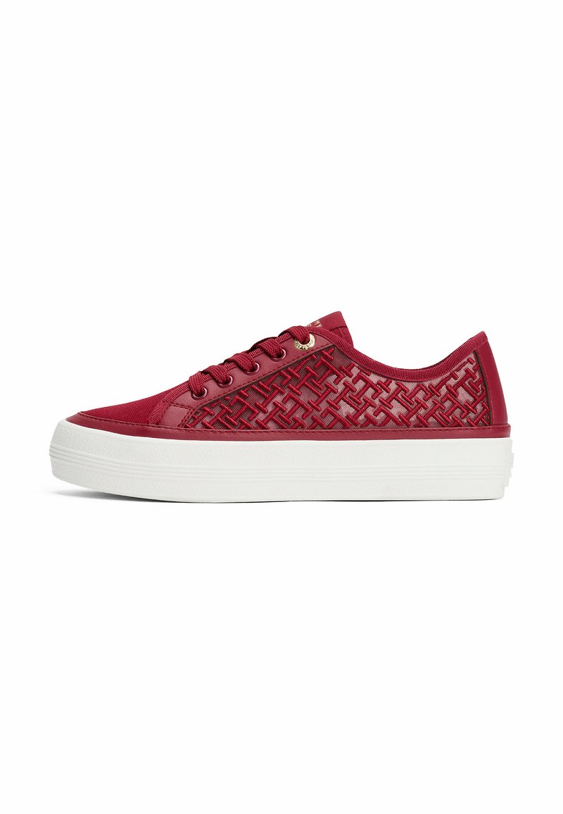 Zapatilla roja con un patrón texturizado en el lateral, suela de goma blanca y seis ojales para los cordones. Acabado de material suave en toda la superficie.