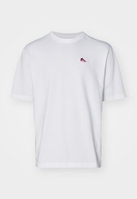 T-shirt bianco in cotone con maniche corte, con un piccolo logo di scarpe da ginnastica rosso e blu sul lato sinistro del petto. Design classico con collo rotondo.