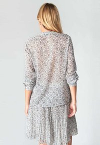 Camicia trasparente a maniche lunghe di colore grigio chiaro con motivo floreale. Vestibilità rilassata e dettaglio plissettato sull'orlo, con maniche arrotolate.