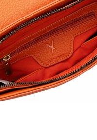Interior de un bolso de cuero texturizado naranja, con un forro naranja brillante, bolsillo con cremallera y detalle del logo en relieve. Cremalleras de alta calidad.