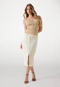 Top a maniche sottili beige a coste abbinato a una gonna cargo bianca con tasche e uno spacco frontale, accentuato con stringhe.