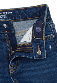 Jeans de mezclilla azul oscuro con cierre de cremallera y botón, que cuentan con costuras en contraste, zonas desgastadas y un forro interior suave.
