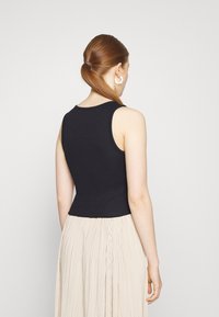 Black sleeveless top in a fitted design, paired with a pleated cream skirt. Smooth fabric texture is visible. Simple neckline and stitching.