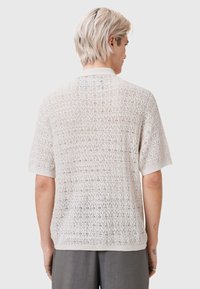 Beżowy krótki sweter z dzianiny z otwartym wzorem koronkowym. Posiada prążkowany kołnierz i mankiety, lekki i oddychający materiał.