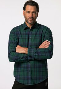 Camisa de franela a cuadros verdes y azul marino con cuello abotonado, mangas largas y un bolsillo en el pecho izquierdo. Textura suave, corte relajado.
