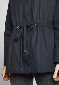 Giacca in nylon con coulisse, vita elasticizzata, occhielli metallici e texture a contrasto. Presenta una finitura liscia e un orlo dritto.