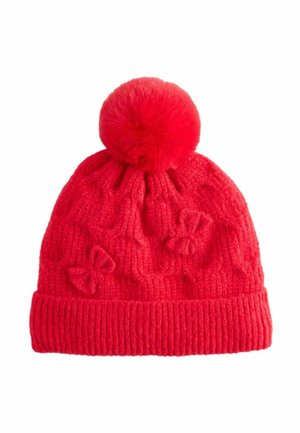 Gorro de punto rojo con puño acanalado, que cuenta con un gran pompón de piel en la parte superior y un patrón texturizado que incluye pequeños lazos a lo largo del cuerpo.