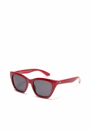 Gafas de sol rojas con montura de ojo de gato y lentes tintadas oscuras, ligeramente inclinadas sobre un fondo blanco.