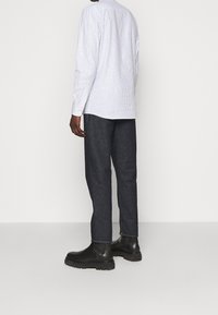 Camicia a maniche lunghe a righe in blu chiaro e bianco, abbinata a pantaloni in denim blu scuro su misura e stivaletti neri con suola robusta.