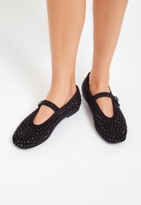 Scarpe flat nere con punta arrotondata e cinturino alla Mary Jane, ricoperte da piccoli chiodi neri per aggiungere texture e dettagli di design.