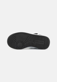 Semelle en caoutchouc noir d'une basket avec des motifs texturés pour l'adhérence et un marquage de la marque "Champion" visible sur la zone du talon.