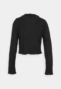 Svart cropped långärmad tröja med en texturerad yta, scallopad halsringning och fåll. Materialet verkar lätt och något skrynkligt.