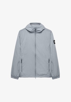 Jachetă ușoară, gri deschis, cu glugă, fermoar complet și două buzunare laterale. Manșete elastice și un mic patch pe mâneca stângă.