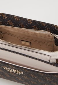 Černá a hnědá vzorovaná kabelka se zlatými doplňky, s světlým interiérem a zipovými přihrádkami. Logotyp značky je viditelný uvnitř.