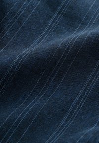 Tissu bleu foncé à fines rayures blanches verticales, montrant la texture et de légers plis.