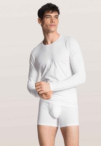 White long-sleeve top and boxer briefs made of smooth, stretchy fabric. The outfit features a fitted design with minimal seams.