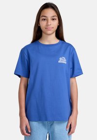 Camiseta de algodón azul con cuello redondo, mangas cortas y un logo impreso en blanco en el pecho. El corte es relajado y casual.