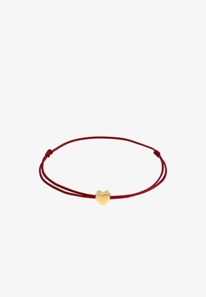 Bracelet en cordon rouge avec un charm en forme de cœur en or, texture lisse, longueur ajustable et détail de nœud sécurisé de chaque côté.