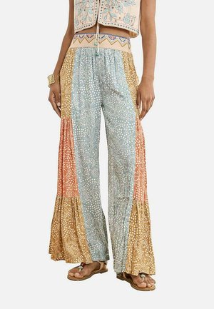 Pantalones anchos y sueltos con patrones florales de patchwork en azul, naranja y mostaza, combinados con sandalias planas con cuentas y un top corto bordado.