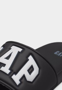 Sandale noire à glissière avec une large bande présentant de grandes lettres blanches en relief « GAP » sur le dessus.