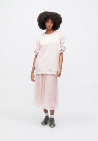 Ροζ φούτερ με λουλουδάτη λεπτομέρεια, σε συνδυασμό με μια αέρινη, διάφανη ροζ τούλινη φούστα και γκρι αθλητικά παπούτσια, δημιουργώντας μια στρωματοποιημένη, απαλή αισθητική.