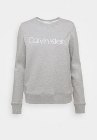 Grauer Pullover aus weichem Stoff, mit langen Ärmeln, Rundhalsausschnitt und dem weißen "Calvin Klein"-Logo, das deutlich auf der Brust prangt.