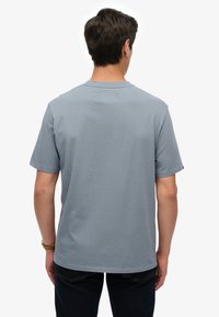 Camiseta de algodón gris claro con mangas cortas, cuello redondo y ajuste relajado. Sin patrones ni gráficos visibles en la parte trasera.