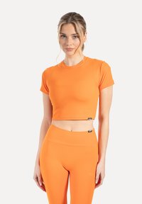 Haut court à manches courtes en tissu orange vif. Design ajusté avec une texture lisse et des étiquettes logo à l'ourlet. Associé à des leggings assortis.
