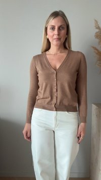 Hnědý pletený kardigán s výstřihem do V, dlouhými rukávy a šesti růžovými knoflíky. Spárováno s bílými kalhotami s vysokým pasem. Neutrální pozadí.