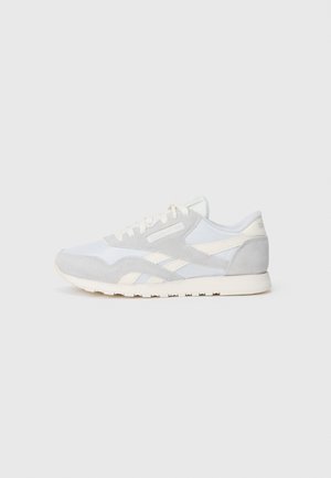 Athletic sneakers in white and light gray suede and mesh. Features a low profile, rounded toe, and contrasting white stripes on the sides.