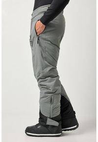 Pantaloni grigi da esterno con un design aderente, dotati di tasche con zip e polsini regolabili, abbinati a stivali invernali neri.