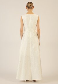 Robe blanche longue jusqu'au sol avec un motif floral texturé, sans manches et fermeture éclair dissimulée dans le dos. Couleur unie, silhouette élégante.
