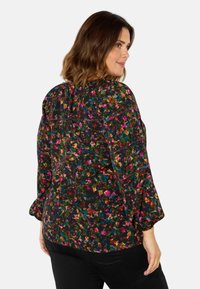 Blusa floreale con sfondo nero, caratterizzata da fiori colorati in tonalità di rosso, rosa, verde e giallo. Vestibilità morbida con maniche a sbuffo.