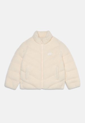 Veste crème, moelleuse avec fermeture éclair, col montant, deux poches avant et petit logo blanc Nike sur la poitrine gauche.