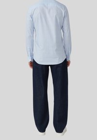 Hellblaues Langarmhemd mit Button-down-Kragen, kombiniert mit locker sitzenden, dunklen Denim-Hosen und weißen Sneakers.